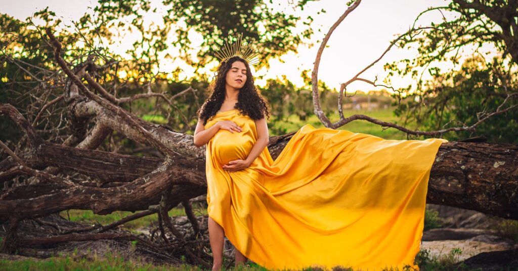 A serene image of a pregnant woman in a yellow gown posing outdoors by a fallen tree.