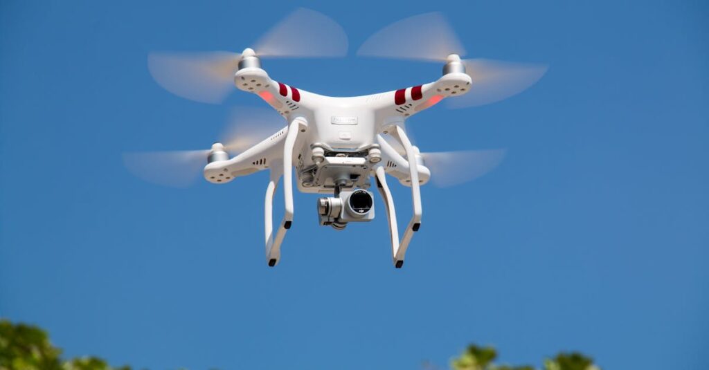 A white drone flying with camera against a clear blue sky.