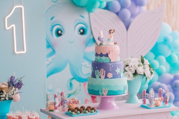 Vibrant mermaid-themed first birthday party decoration with cake, balloons, and sweets.